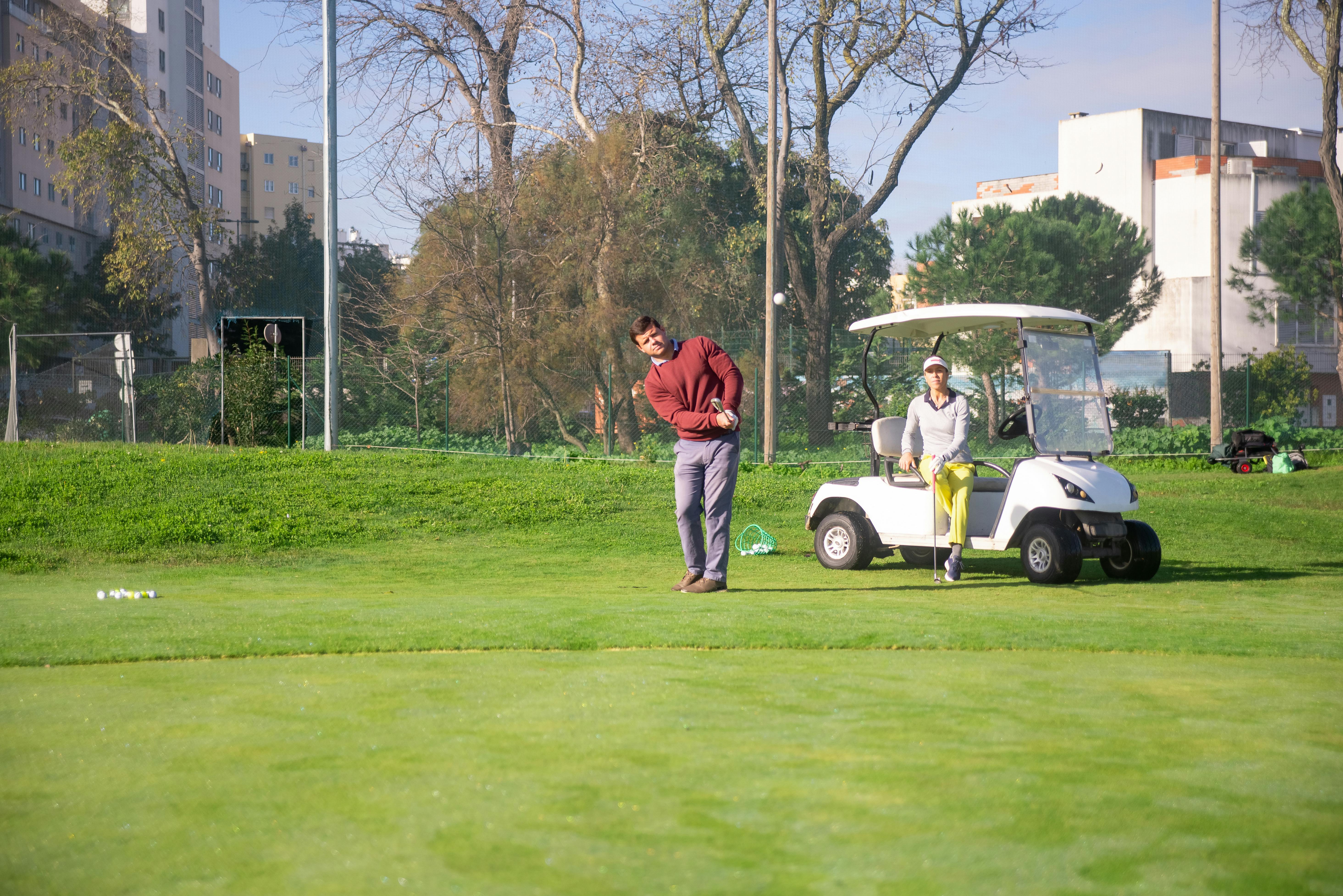 a woman sitting on golf cart while looking at the man playing golf