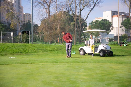 Free A Woman Sitting on Golf Cart while Looking at the Man Playing Golf Stock Photo
