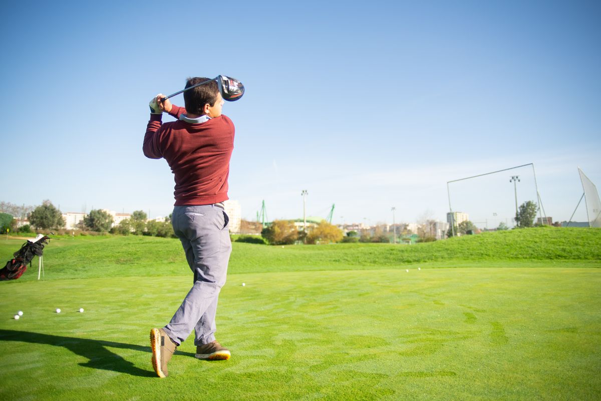 Golfer practicing on the course with a golf bag nearby