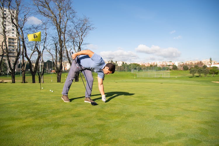 A Man Bending Forward While Holding A Golf Club