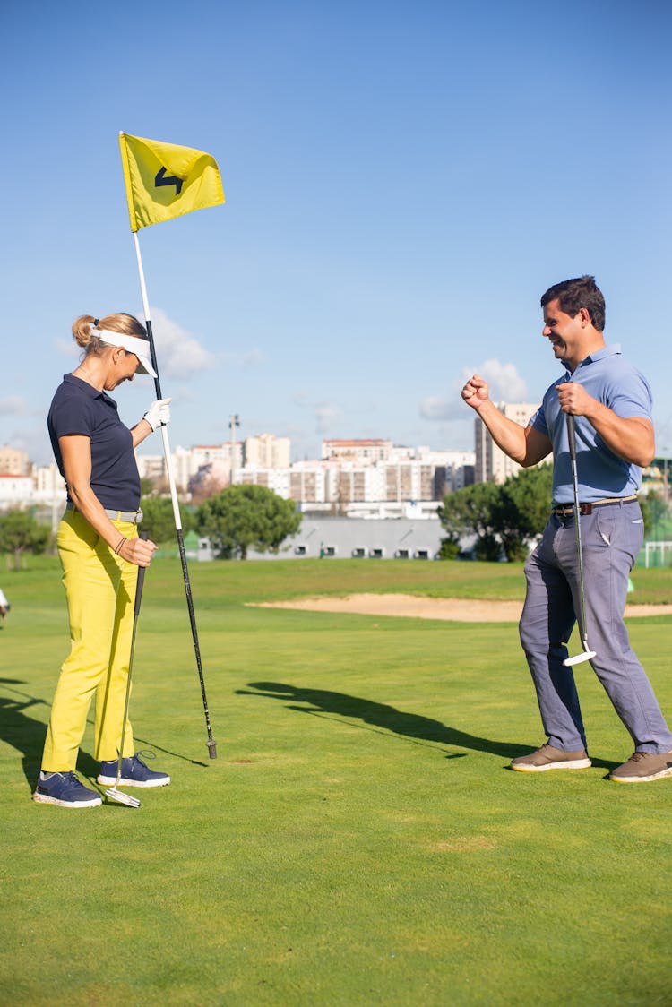 A Man And Woman Standing On The Field While Holding Golf Club