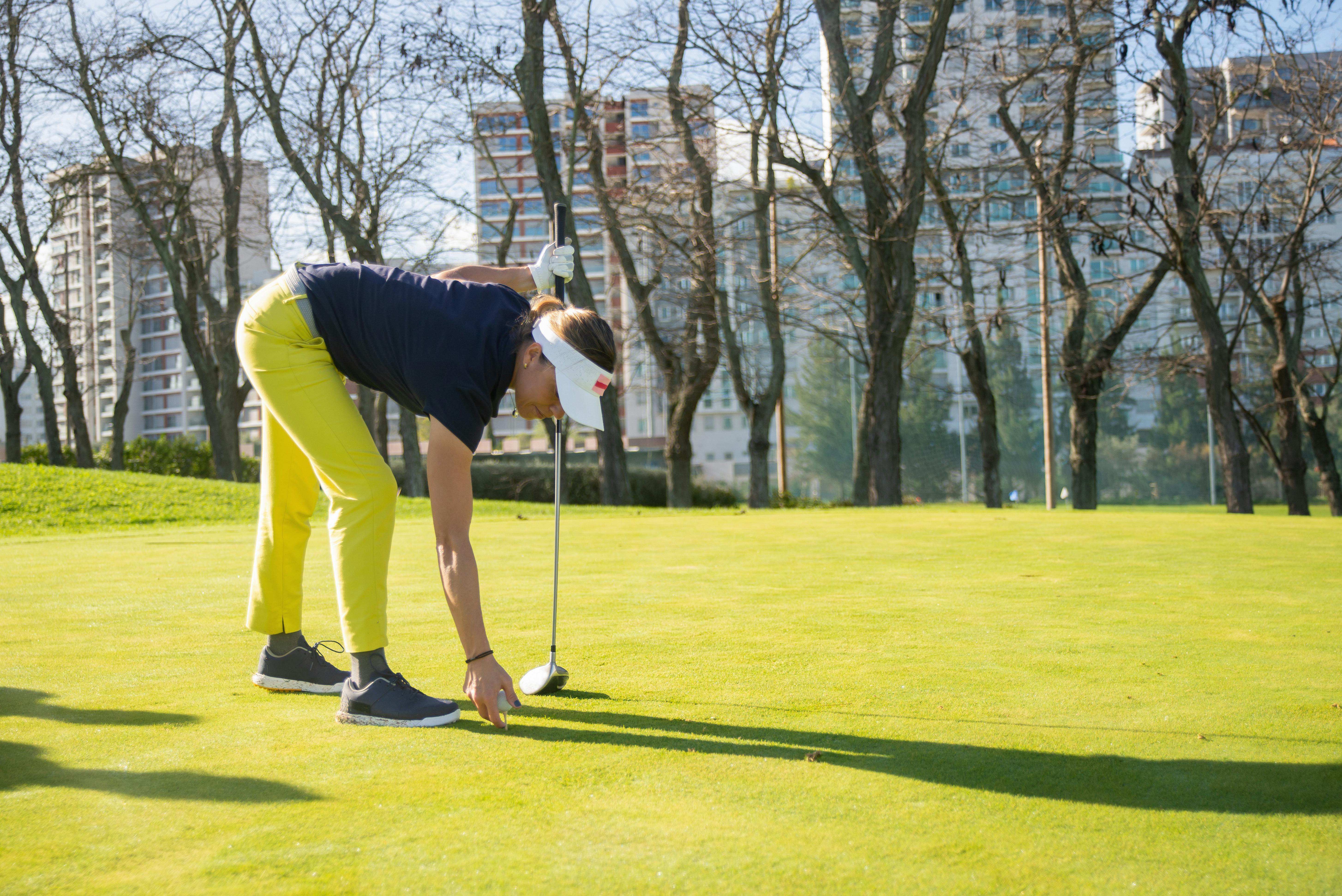 a woman in yellow pants bending forward while holding a golf ball