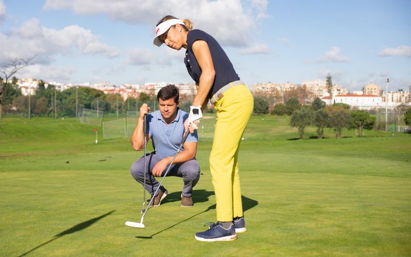 A golfer receiving hands-on instruction from a PGA professional during a lesson at a well-maintained European golf course, with the coach observing the student's stance and grip closely.