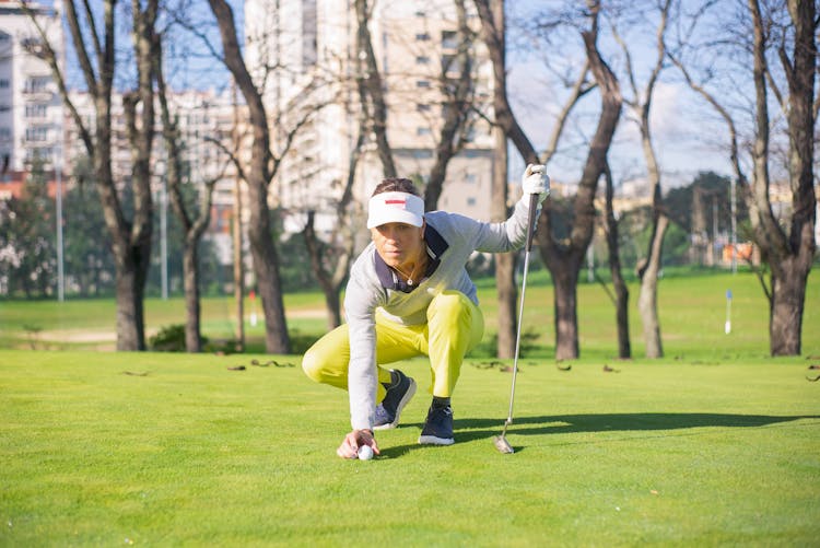 A Woman In Yellow Pants Sitting While Holding A Golf Club And A Ball On Green Grass