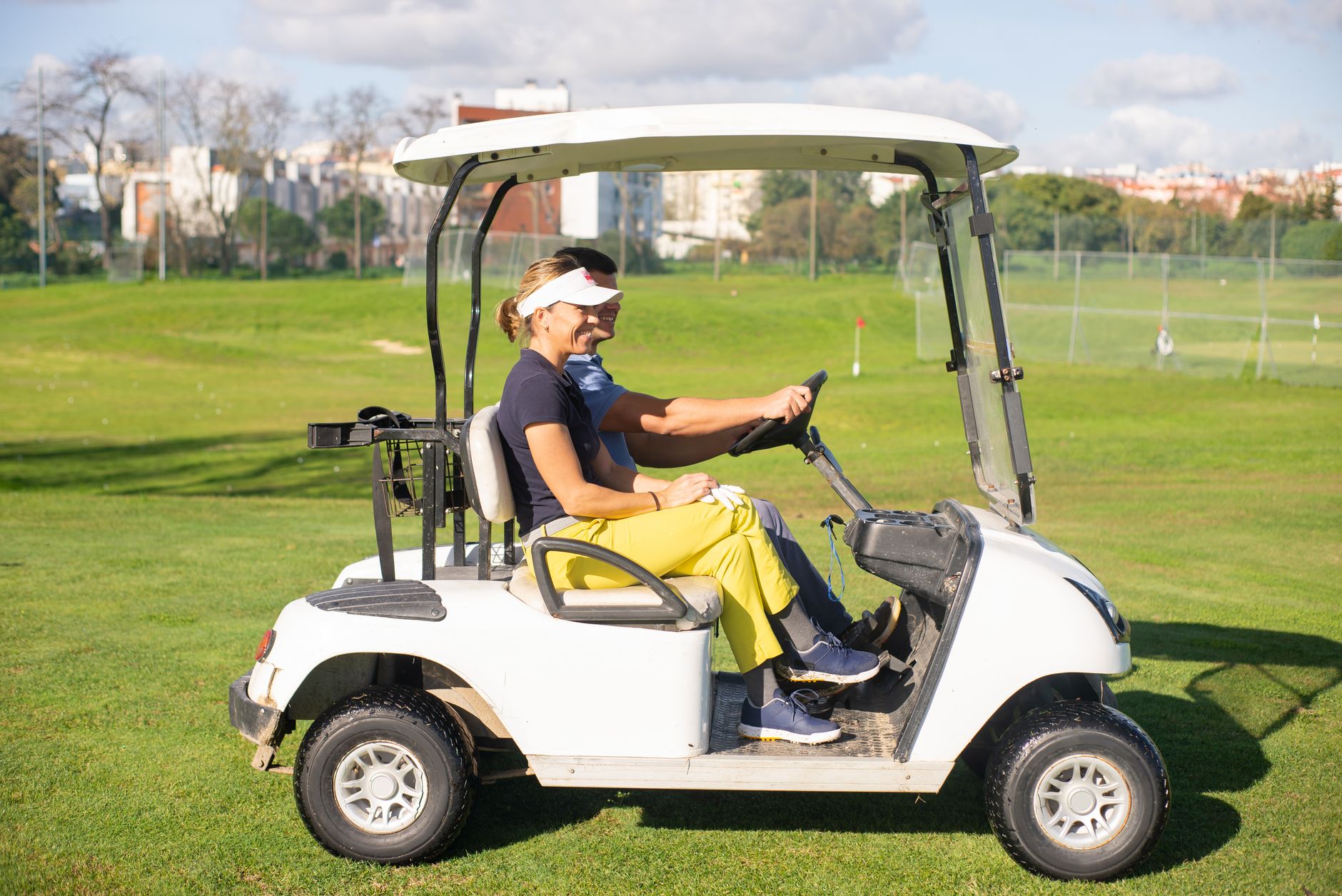 A couple driving a golf cart on a sunny day at a golf course. Perfect for lifestyle and leisure themes.