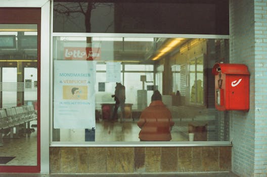 Through glass of anonymous tourists in warm outerwear standing in waiting room of modern railway station
