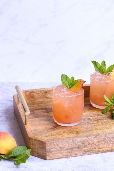 A bottle of peach schnapps next to a glass of peach-colored cocktail garnished with a peach slice and fresh mint