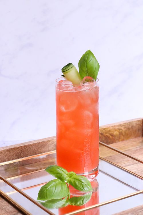 Free Glass of bright tasty cocktail with fresh basil leaves on ice reflecting on square shaped tray Stock Photo