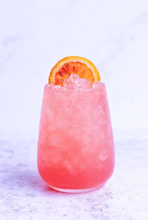 Free Glass of delicious pink beverage with ice and fresh orange slice on marble surface Stock Photo