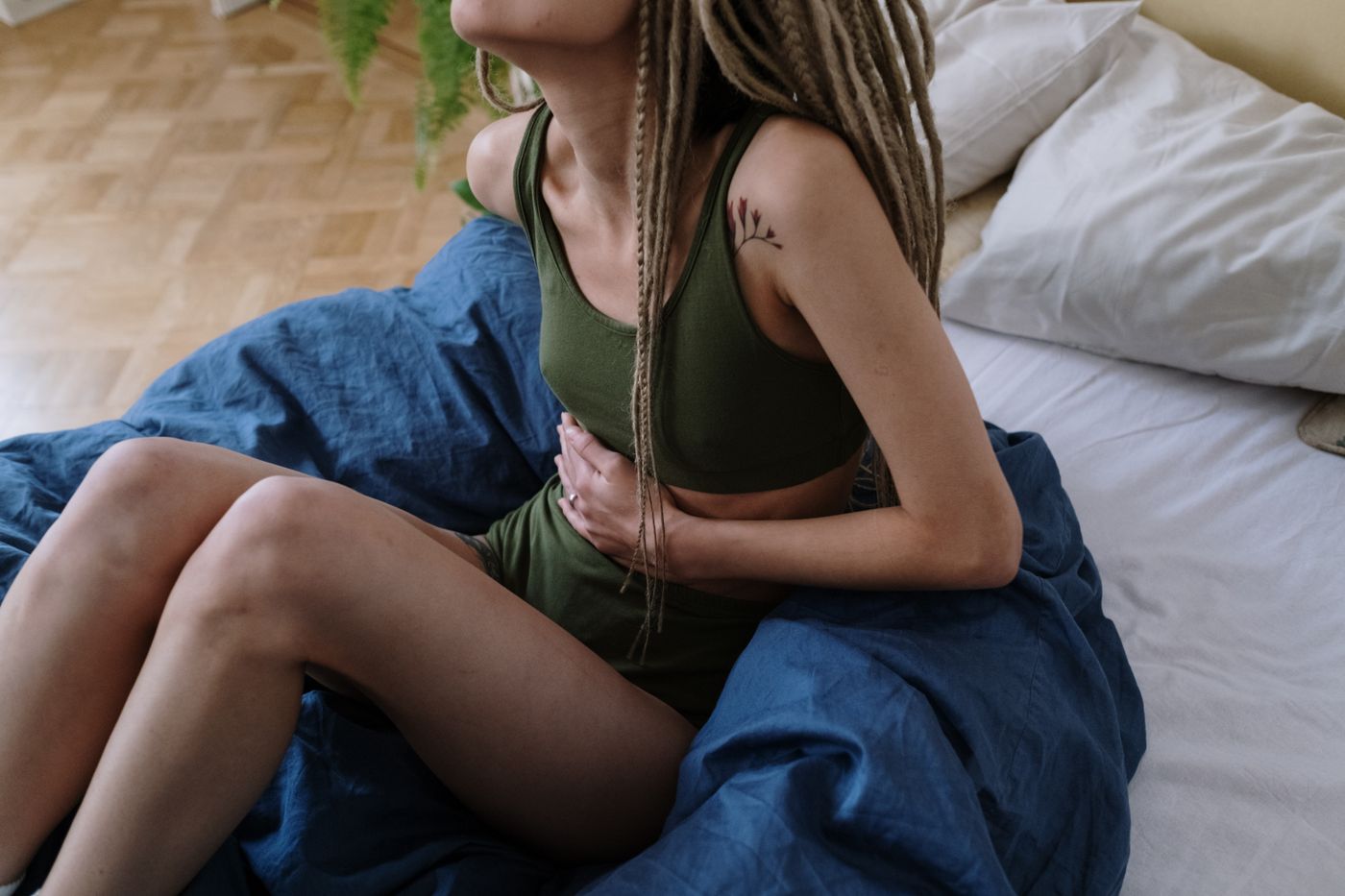 Young woman sitting on bed in pain holding her stomach — severe menstrual cramps and endometriosis, the pain Olivia normalized for years