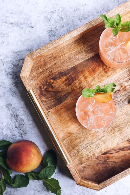 Top view arrangement of delicious icy berry drink decorated with mint and served on wooden tray near ripe peach