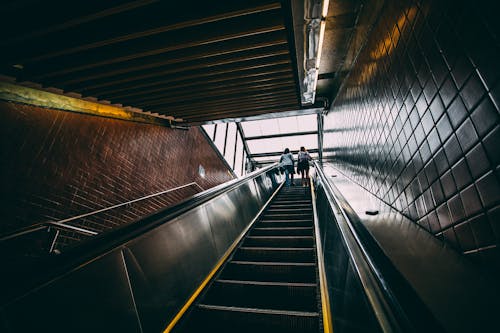 2 Person Standing on Black Escalator during Daytime