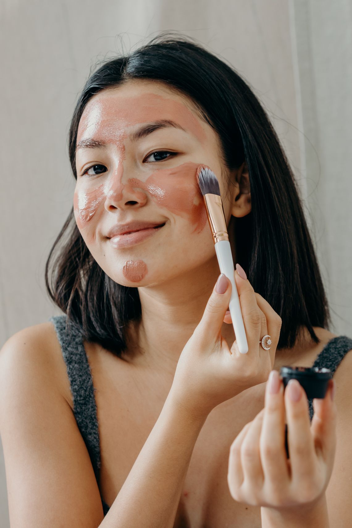 Smiling woman applying a facial beauty mask with a cosmetic brush