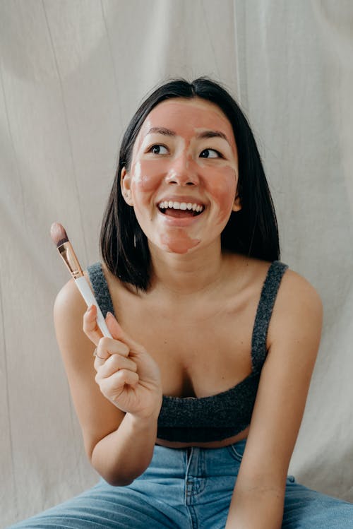 A Woman in Gray Tank Top Sitting while Holding a Makeup Brush