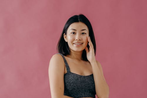 Free A Woman in Gray Tank Top Smiling while Touching Her Face Stock Photo
