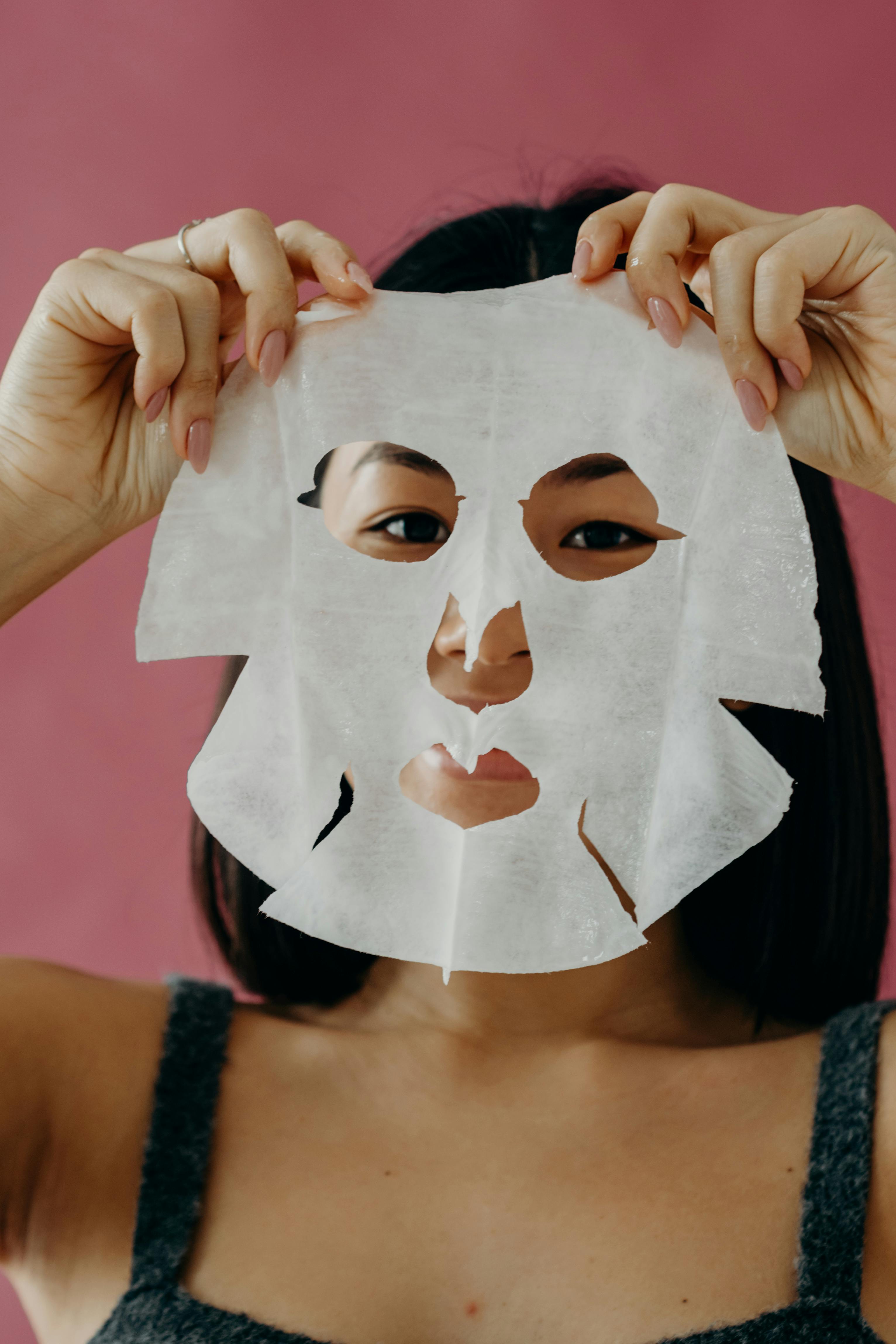 a woman in gray tank top holding a face mask near her face