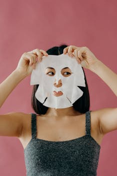 A woman holding a sheet mask over her face, highlighting skincare and self-care routines.