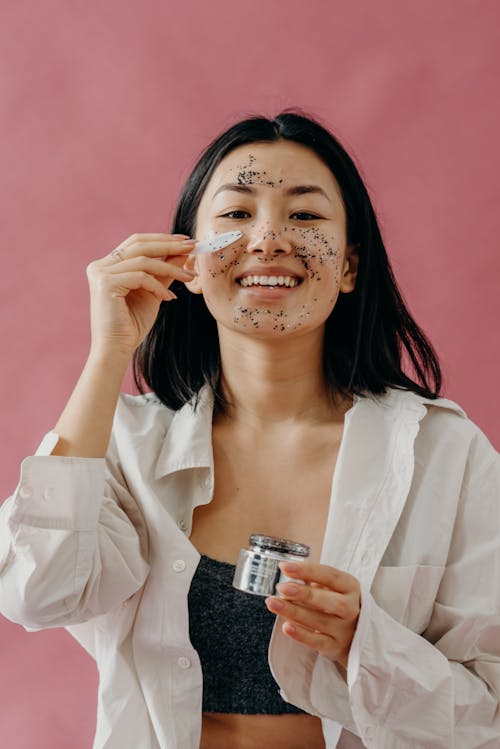 A Woman in White Long Sleeves Applying Glitter Mask on Her Face