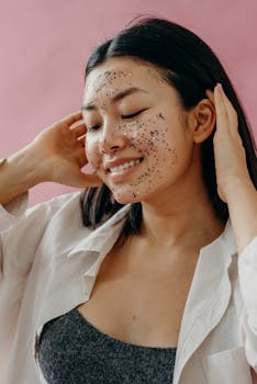 Smiling woman applying a glitter facial mask for skincare routine.