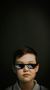 Studio portrait of a child wearing pixelated sunglasses against a dark background.