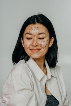 Asian woman wearing a glitter exfoliating face mask, smiling softly as part of her skincare routine.