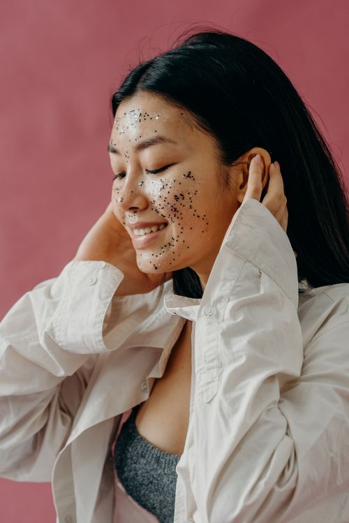 Free Young woman smiling with a glittery facial mask against a pink background, showcasing beauty and skincare. Stock Photo
