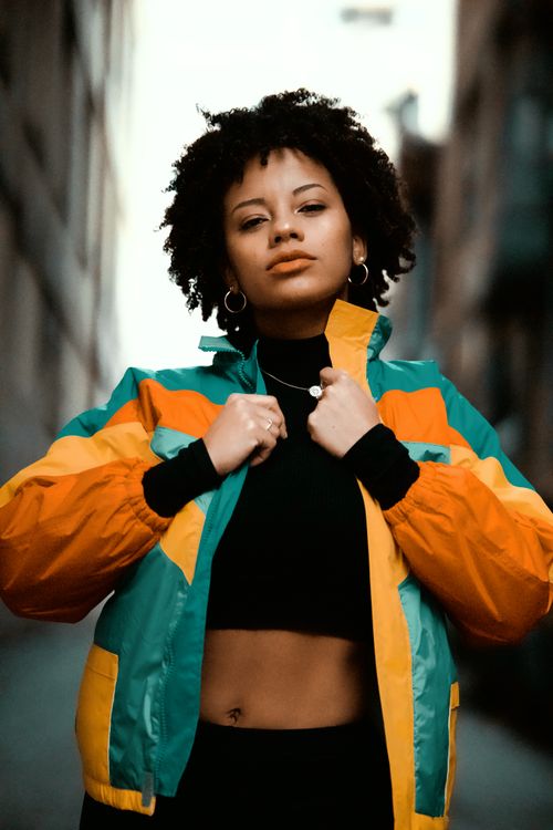 Free Confident woman standing outdoors, showcasing vibrant jacket and street fashion style. Stock Photo