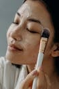 一位亚洲女性的特写镜头正在享受日常护肤，用化妆刷涂抹面霜，以保持皮肤健康