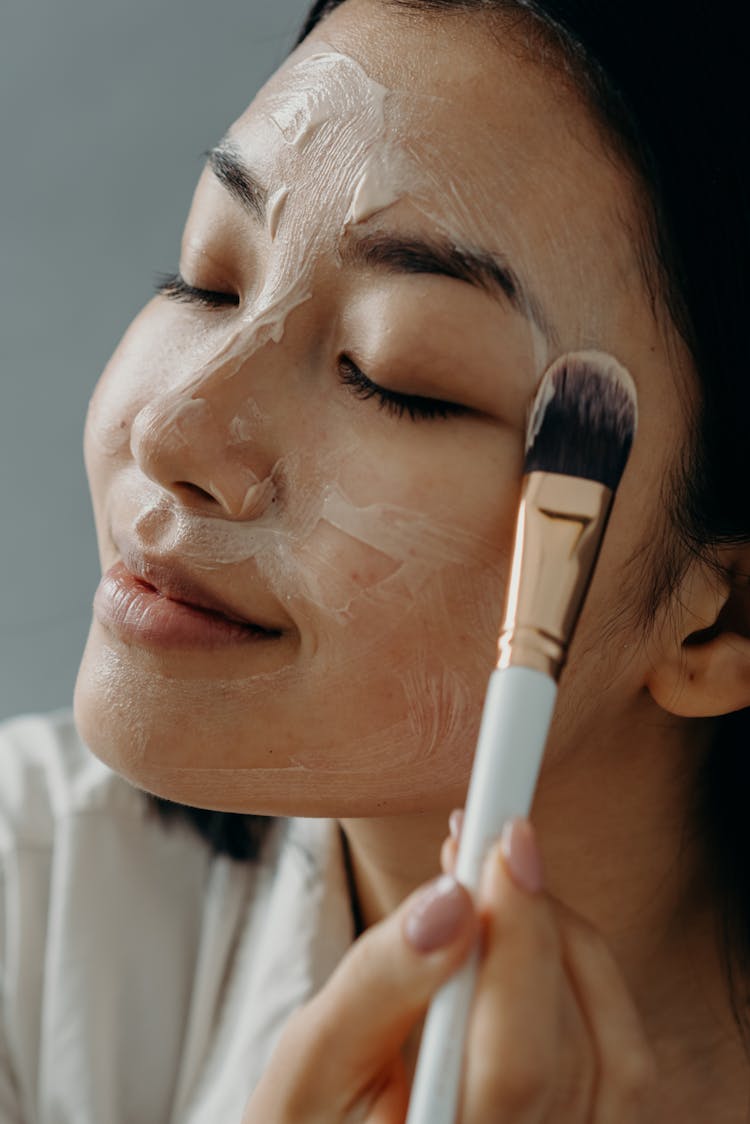 A Woman Applying A Cream On Her Face With Her Eyes Closed