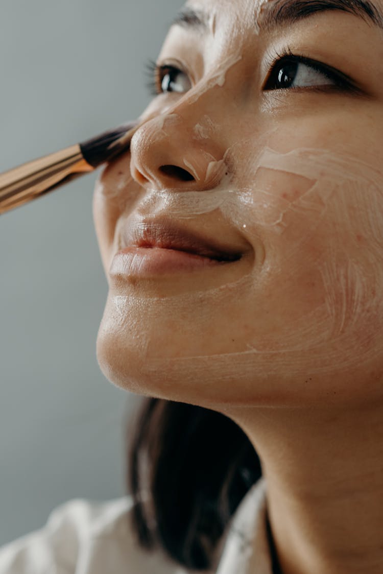 A Close-up Shot Of A Woman Applying A Cream On Her Face