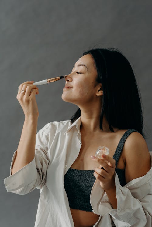 A Woman Applying a Cream on Her Face Using Makeup Brush