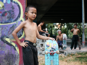 A Shirtless Young Boy Leaning on the Wall while Holding His Skateboard