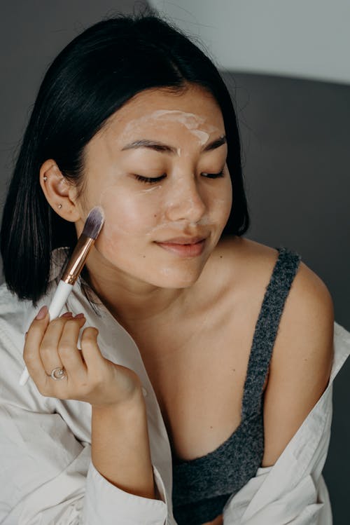 A Woman in Gray Tank Top Applying a Cream on Her Face