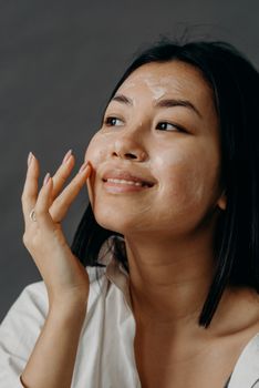 An Asian woman applying a facial cream as part of her self-care routine for healthy skin.