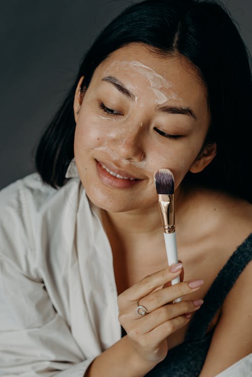 A Woman Applying a Cream on Her Face Using a Brush