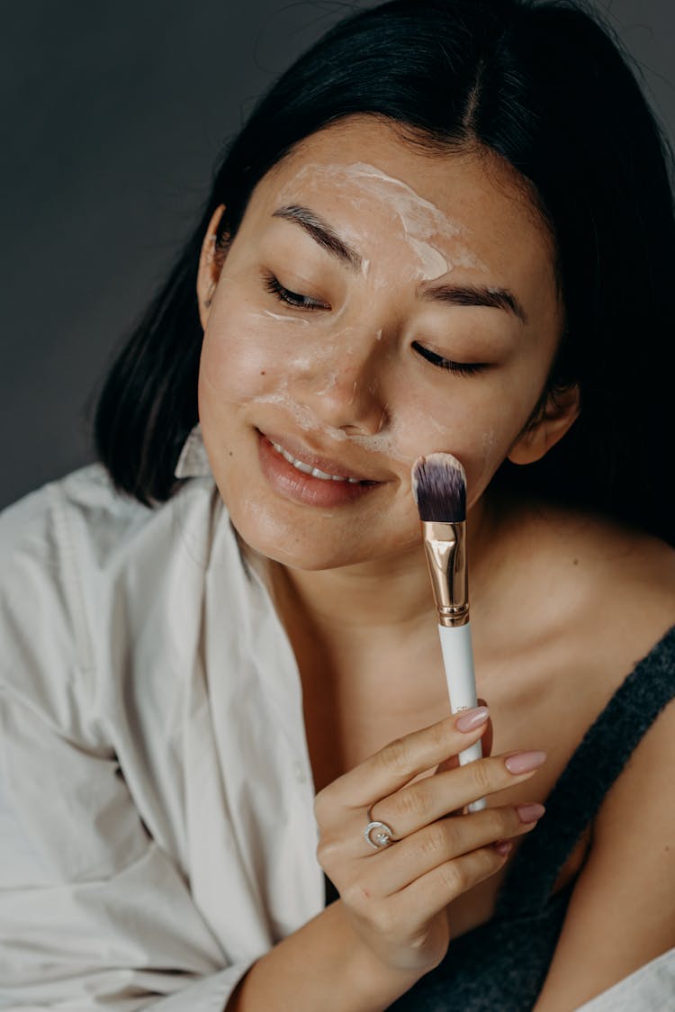 A Woman Applying A Cream On Her Face Using A Brush