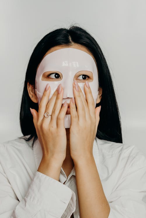 A Woman in White Long Sleeves Wearing Facial Mask with Her Hands on Her Face