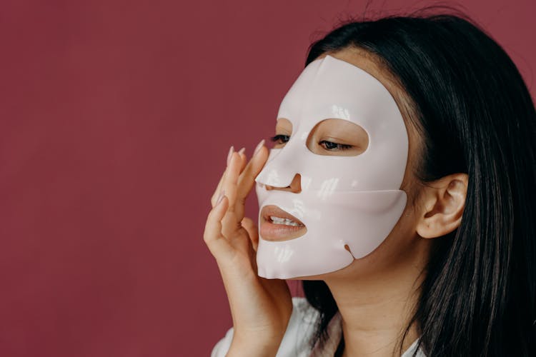 A Woman Touching Her Face With Sheet Mask
