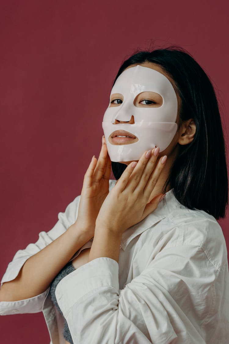 A Woman In White Long Sleeves Touching Her Face With Mask