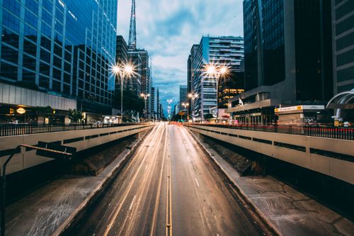 Free A bustling urban street scene at twilight featuring light trails from traffic, framed by tall modern buildings. Stock Photo