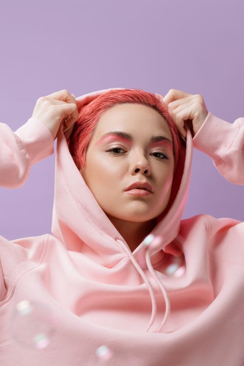 Free Portrait of a woman with pink hair and hoodie against a violet background, exuding confidence. Stock Photo