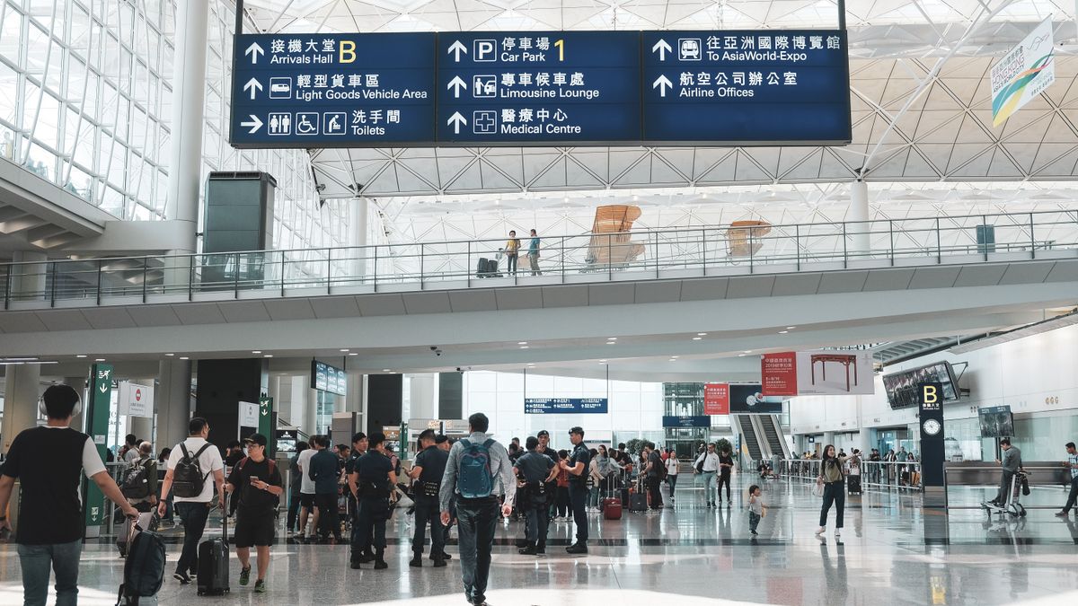 Crowded scene inside Hong Kong International Airport terminal with travelers and signage.