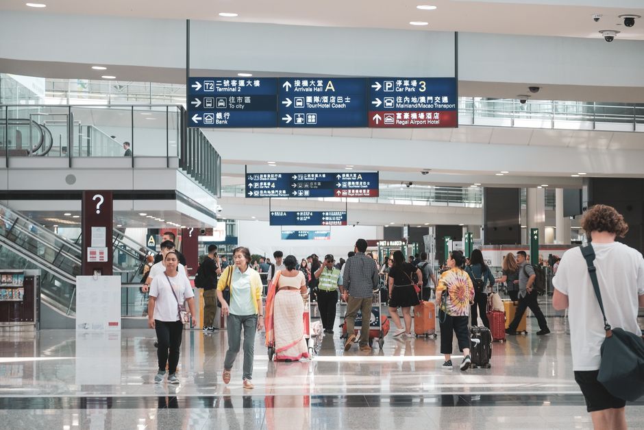 Crowded Hong Kong airport terminal with diverse passengers and informative signage.