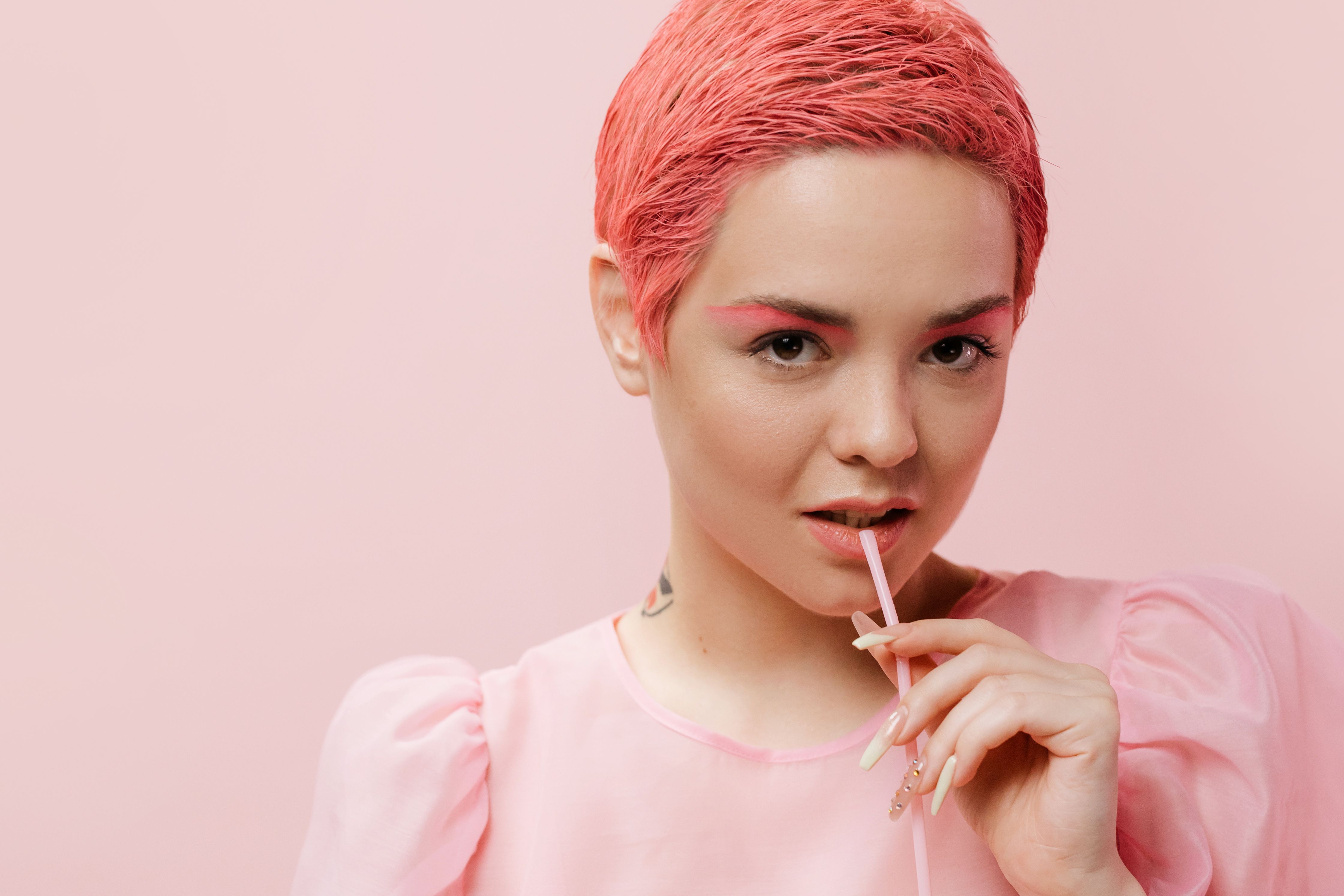 A trendy young woman with pink hair poses confidently in a studio setting, showcasing modern fashion.