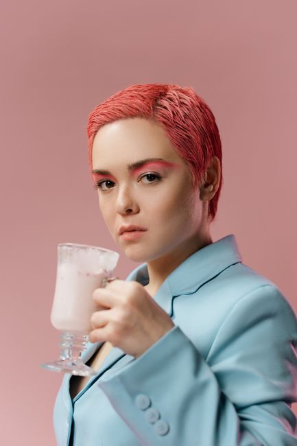 Stylish portrait of a woman in a blue suit holding a cocktail against a pink background.
