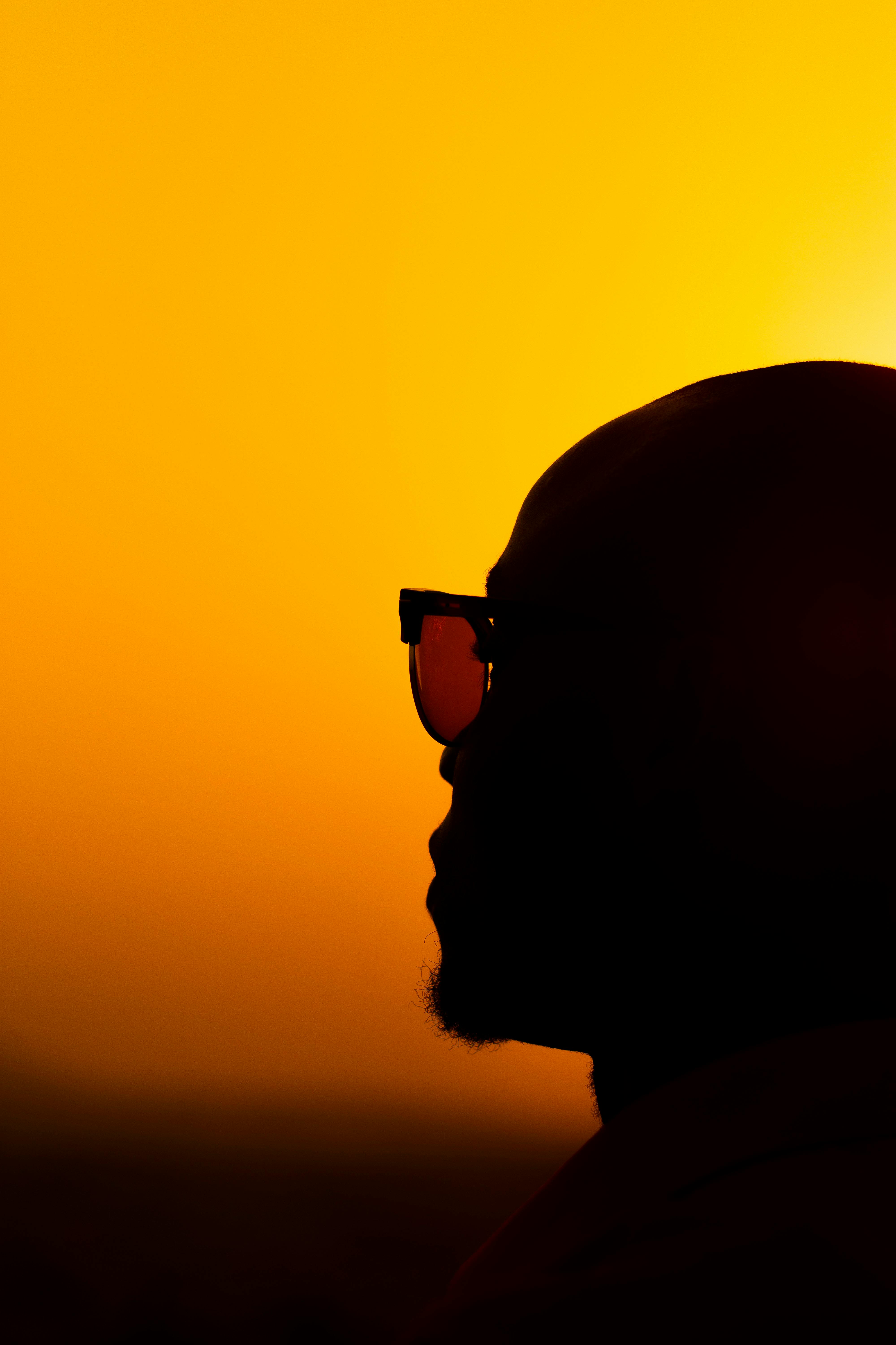 Dramatic silhouette of a man wearing sunglasses against a vibrant, golden sunset. Perfect for artistic themes.