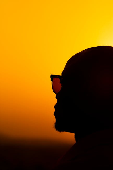 Dramatic silhouette of a man wearing sunglasses against a vibrant, golden sunset. Perfect for artistic themes.