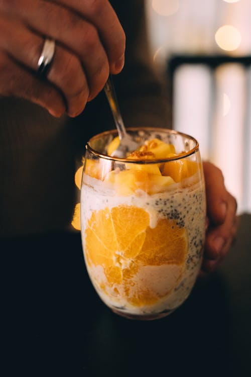 Free Person Holding a Glass of Mango and Orange Chia Pudding Stock Photo