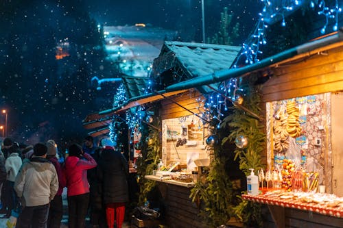 Crowd of many people entertaining near Christmas cafe decorated with shiny baubles and glowing garland