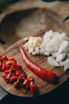 Chopped onions, bell pepper, and garlic on a rustic cutting board, ideal for cooking preparation images.